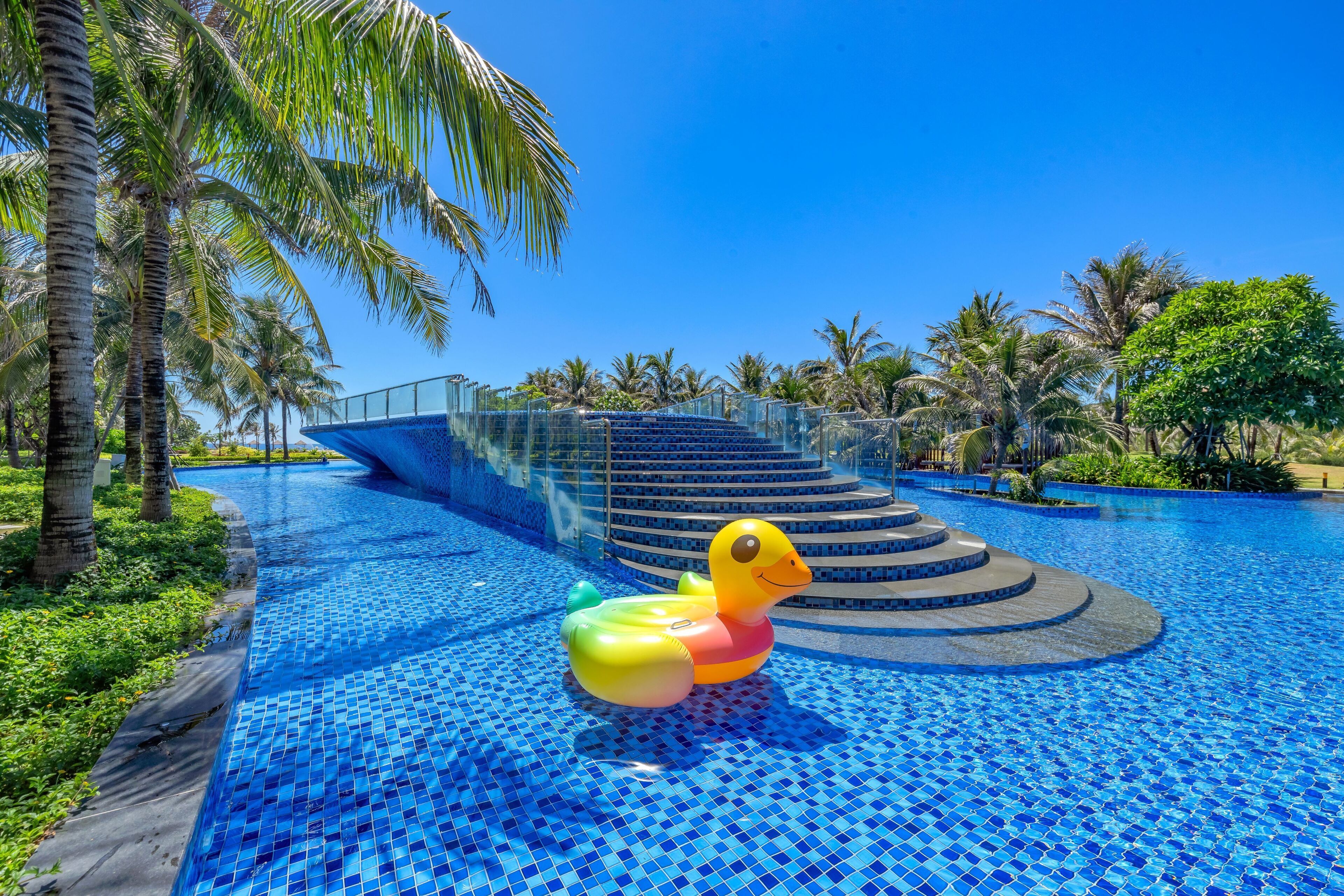 A swimming pool with a duck float, palm trees, and a staircase leading to a higher level.