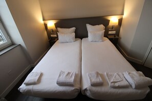 Un lit double avec du linge de lit blanc et des oreillers, deux tables de chevet avec des lampes et une fenêtre avec des stores.