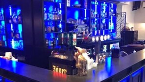 Un espace bar avec un éclairage bleu, des étagères remplies de bouteilles et une caisse enregistreuse.