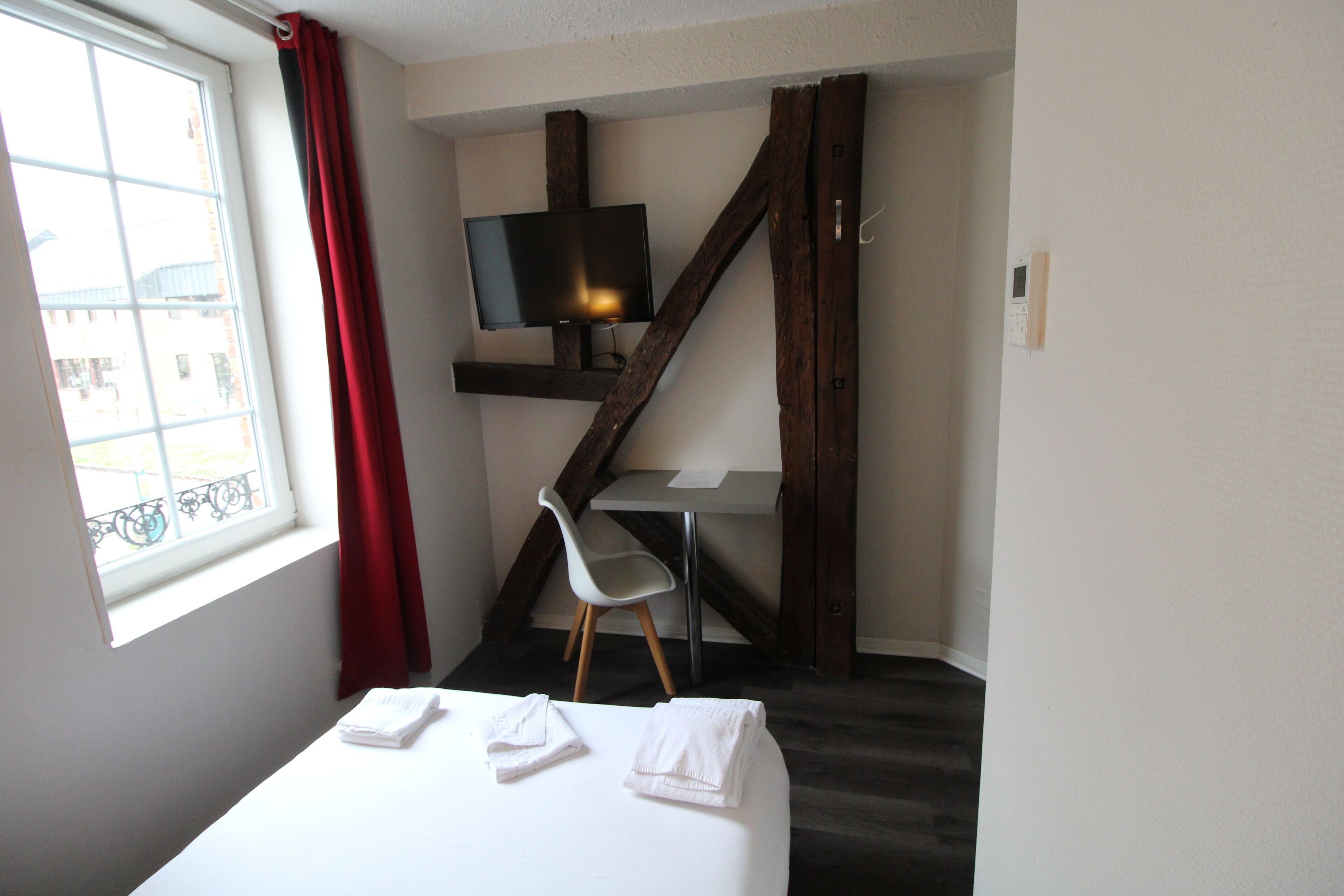 Ein Hotelzimmer mit Bett, Schreibtisch, Stuhl, Fernseher und einem Fenster mit Vorhängen.