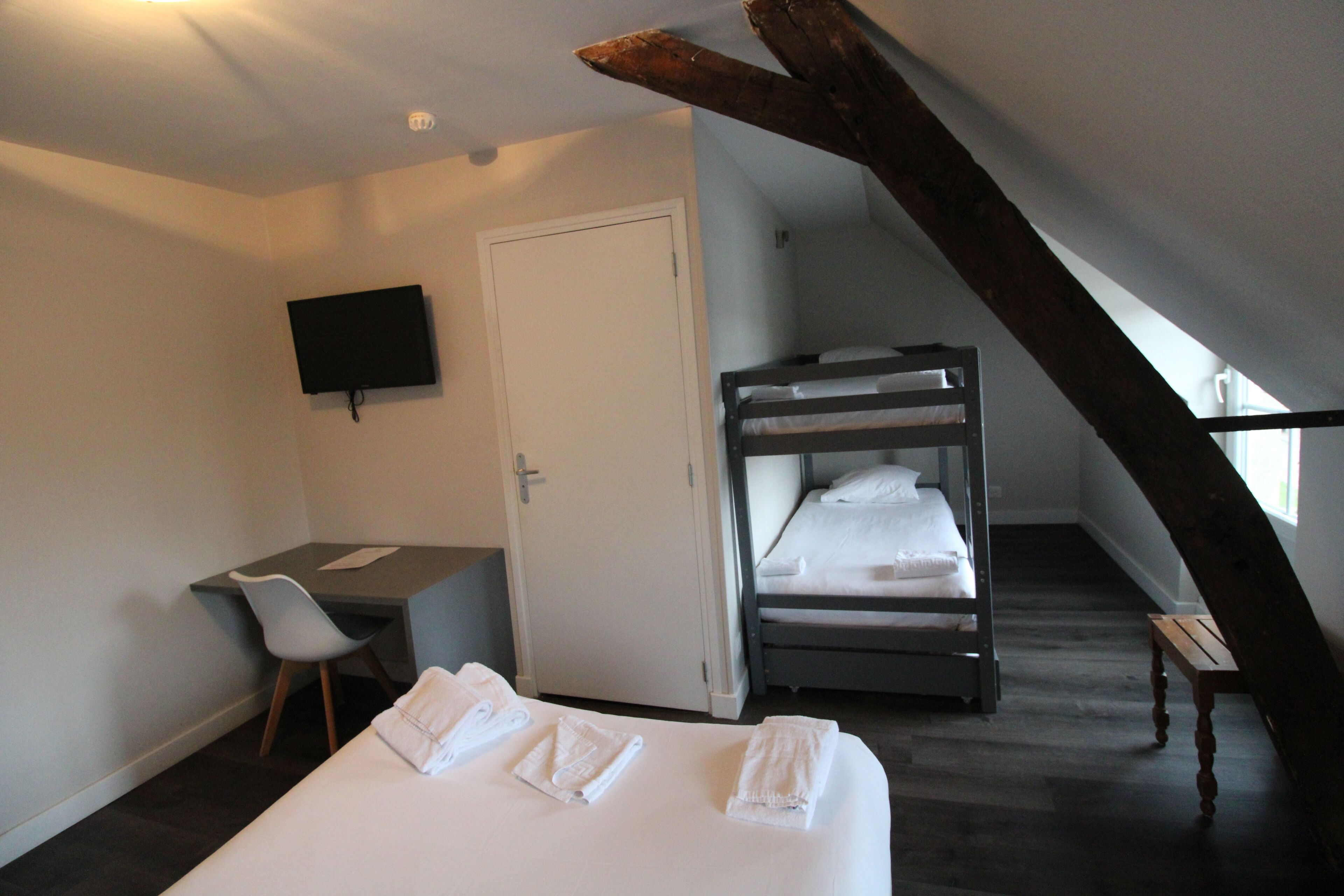 Et hotelværelse med køjeseng, skrivebord med stol, fjernsyn på væggen og en trappe.