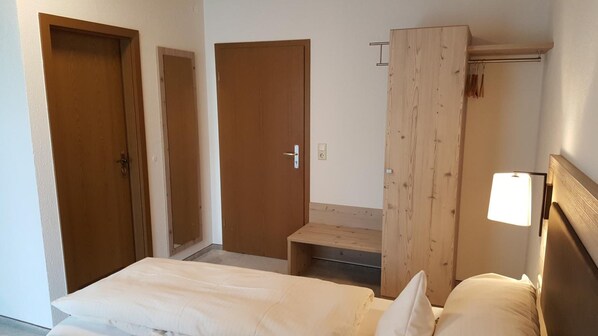 Una habitación de hotel pequeña y de un solo ambiente, con cama, un banco y un armario de madera.