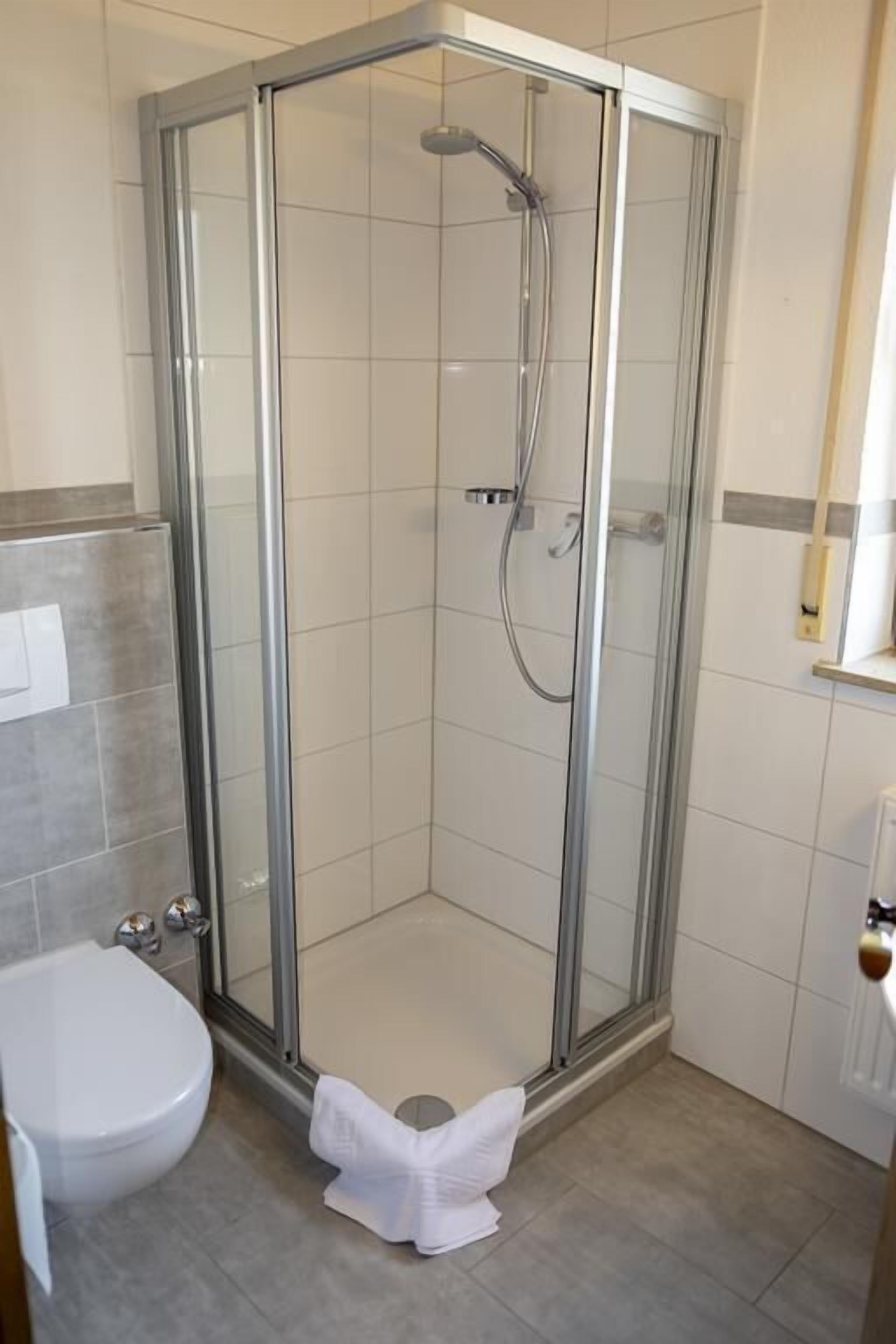 A corner shower enclosure with a glass door, a white toilet, and a towel on the floor.