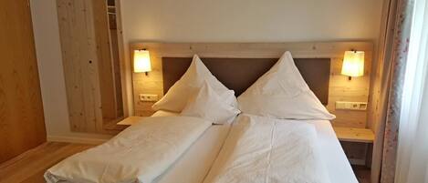 A double bed with white linens, two bedside tables with lamps, and wooden headboard.