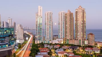 Una zona residencial de rascacielos con edificios modernos, una calle bien iluminada y un mar tranquilo al fondo.