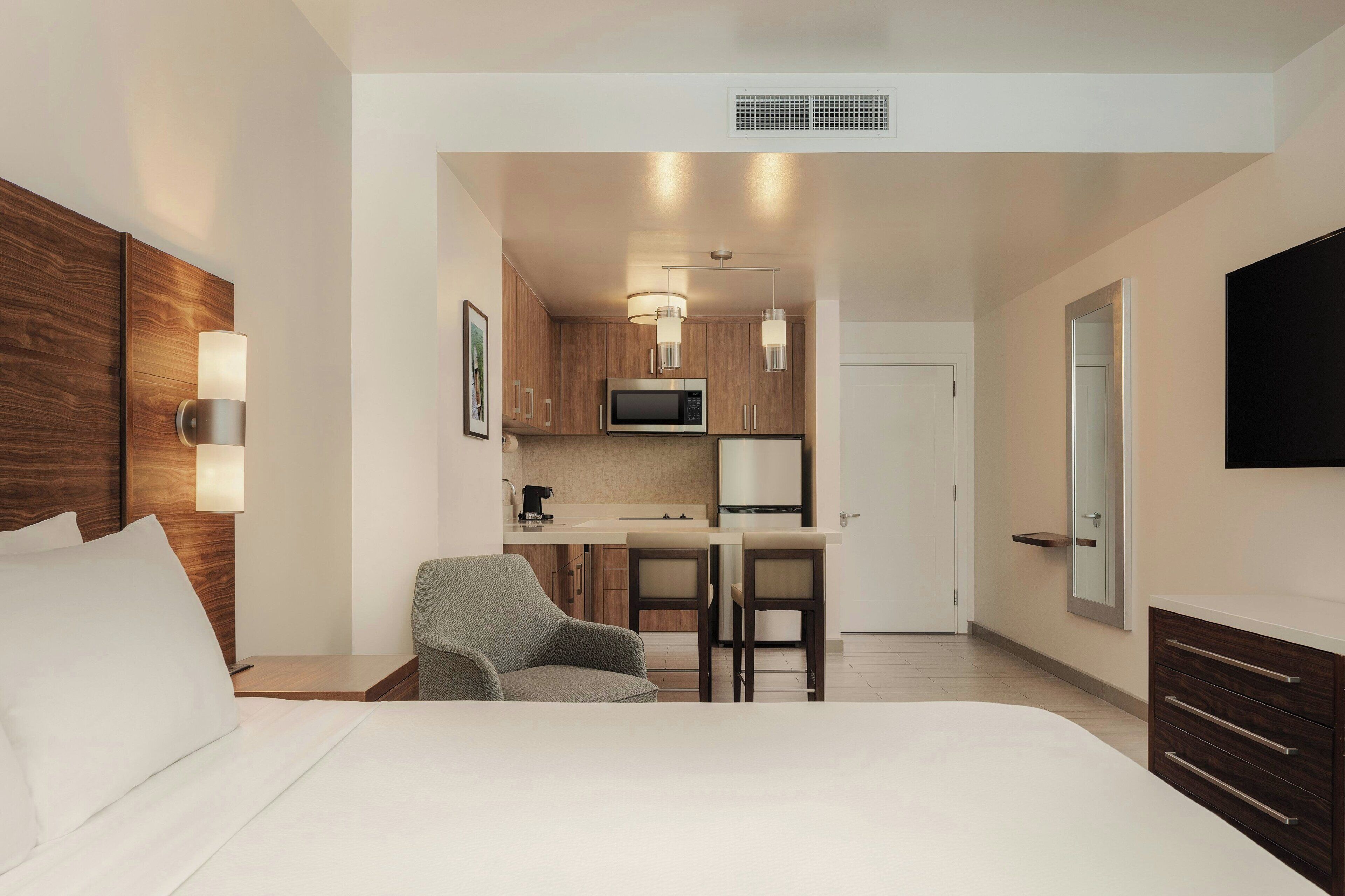 Une chambre d’hôtel comprenant un lit, un bureau avec deux chaises, une kitchenette, une télévision et une armoire.