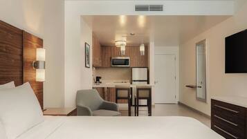 Une chambre d’hôtel comprenant un lit, un bureau avec deux chaises, une kitchenette, une télévision et une armoire.