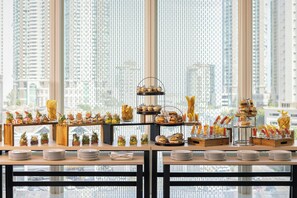 Un buffet proposant une variété de plats et d’ustensiles, disposés sur des tables avec une vue sur le paysage urbain en arrière-plan.