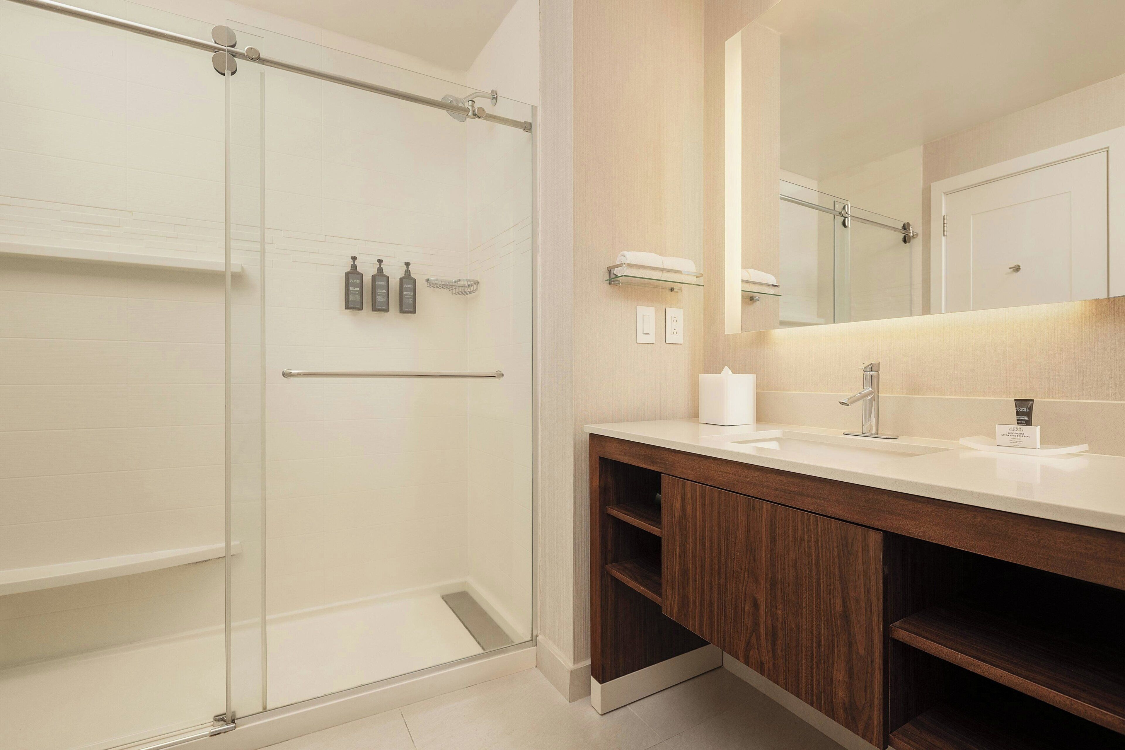 Une salle de bain moderne avec une douche à parois de verre, un meuble-lavabo en bois avec un miroir et un lavabo blanc.