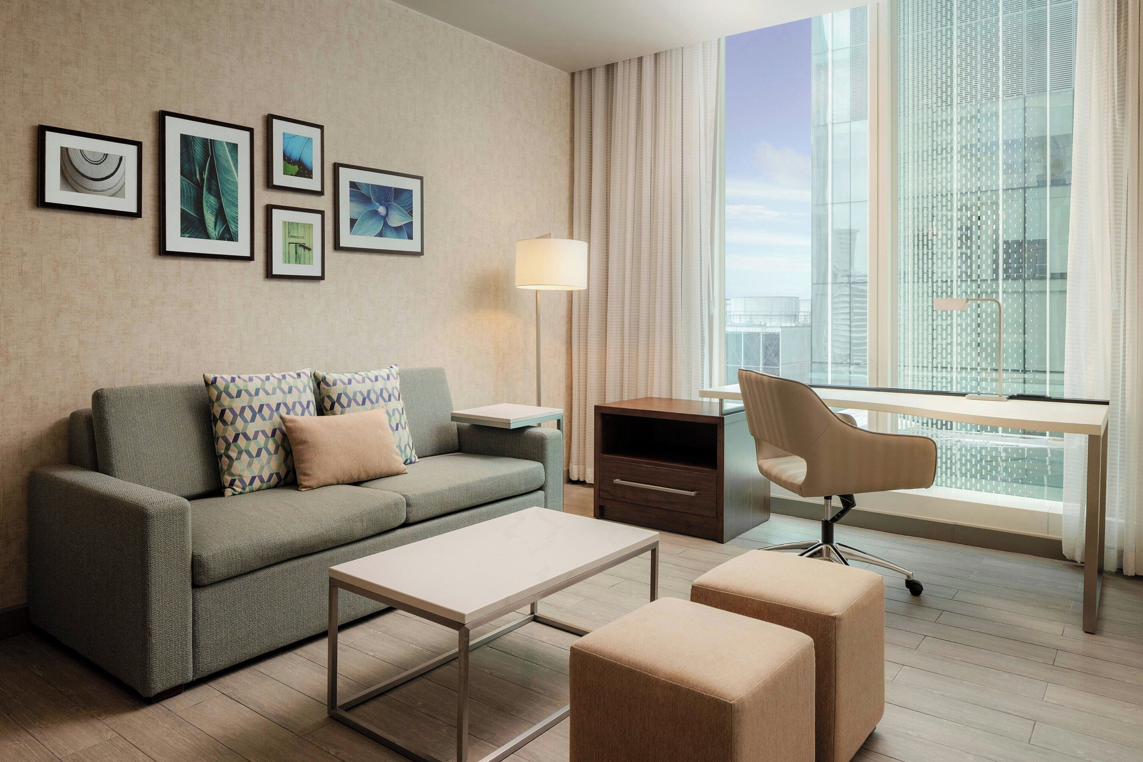 Ein modernes Hotelzimmer mit Sofa, Schreibtisch, Stuhl, Lampe und gerahmten Bildern an der Wand.