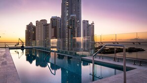 Une piscine moderne d’hôtel, séparée du reste par une paroi de verre, entourée de gratte-ciel et offrant une vue sur le coucher du soleil.