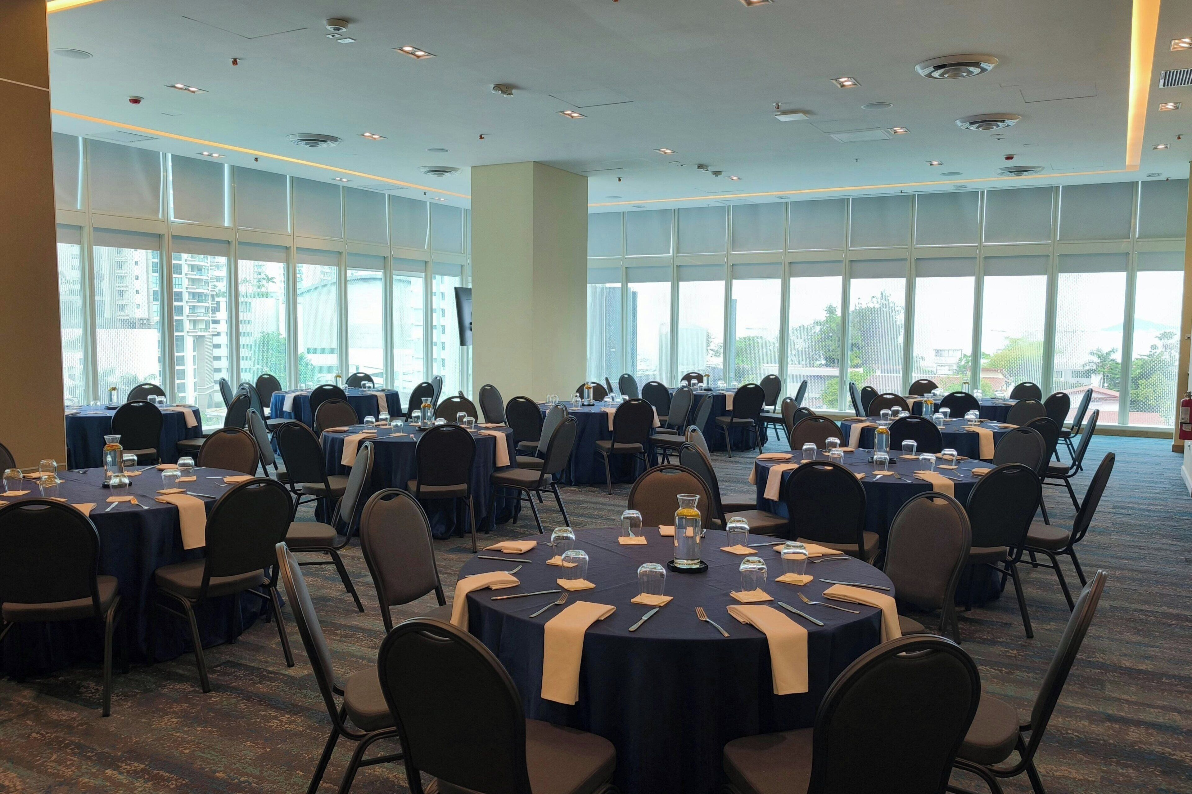 Une salle de conférence dotée de plusieurs tables et chaises, de grandes fenêtres et d’un téléviseur à écran plat.