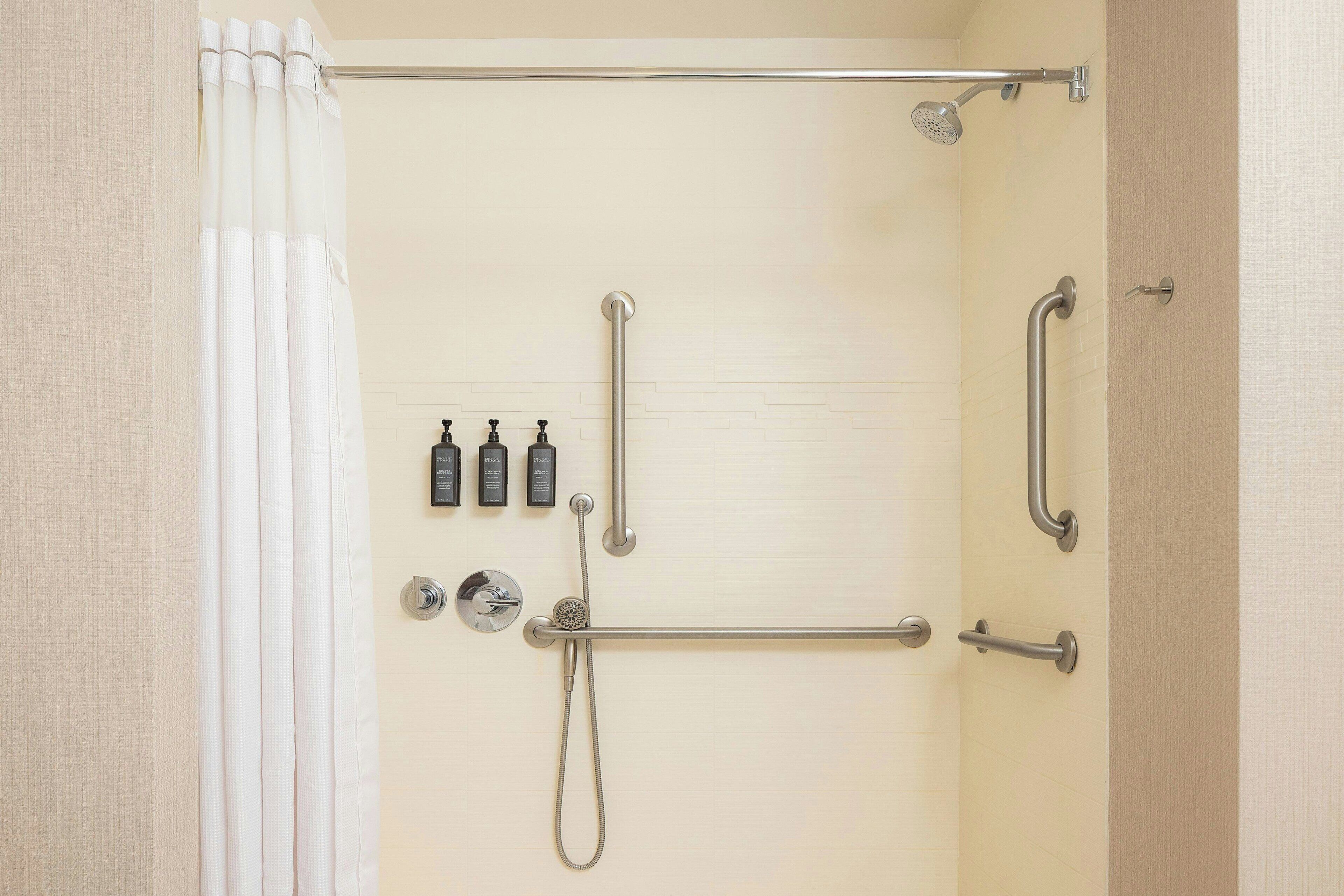 A bathroom with a shower, grab bars, and a hand dryer.