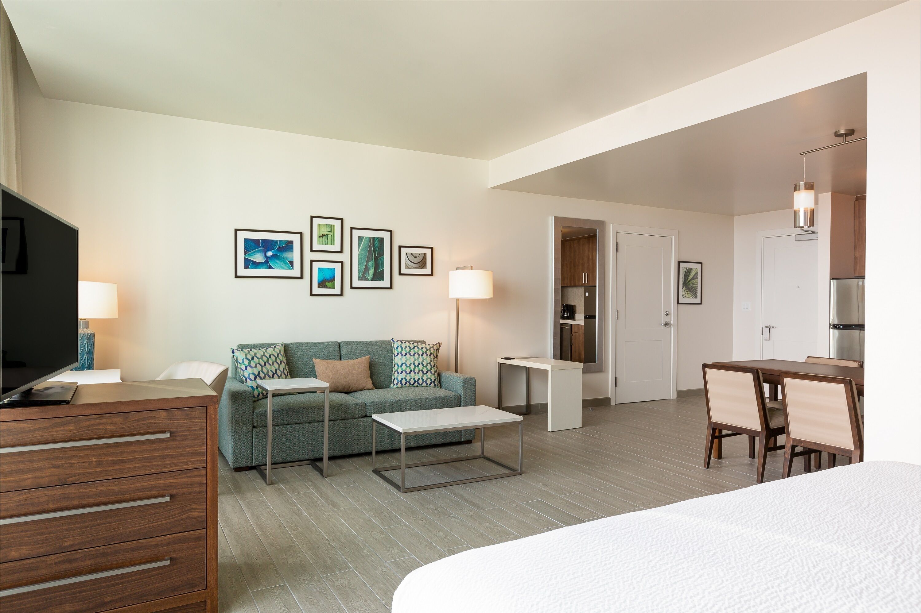 Une chambre d’hôtel moderne équipée d’un canapé, d’une petite table, d’une télévision, d’un bureau et d’une kitchenette.