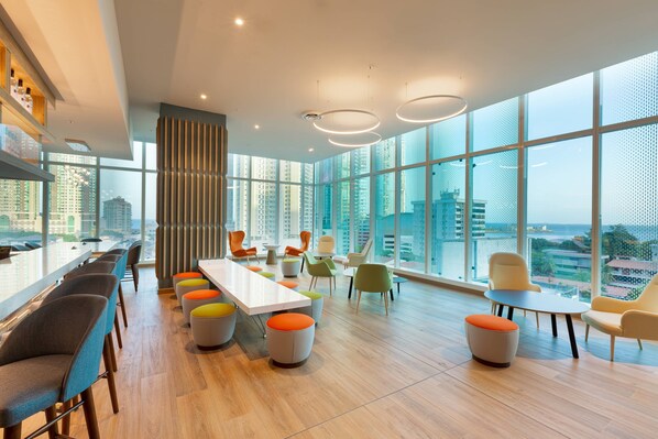 Un moderno salón de conferencias con una larga mesa, sillas coloridas y ventanas amplias con vistas a la ciudad.