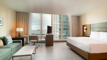 A hotel room with a bed, a desk, a chair, a sofa, and a window with curtains.