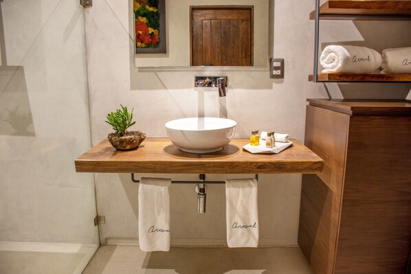 A bathroom with a wooden vanity, a white sink, a small potted plant, and towels hanging from the sink.