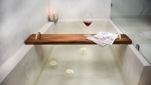 A bathtub with a wooden tray holding a glass of red wine and a magazine.