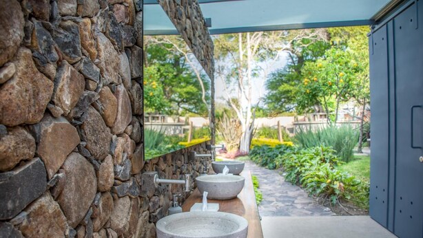 A stone wall with a wooden countertop and three large stone sinks.