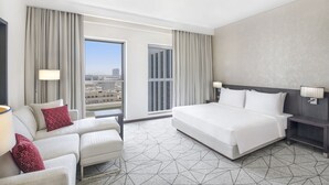 Quarto de hotel com uma cama grande, um sofá, uma mesa de cabeceira e vista da cidade pela janela.