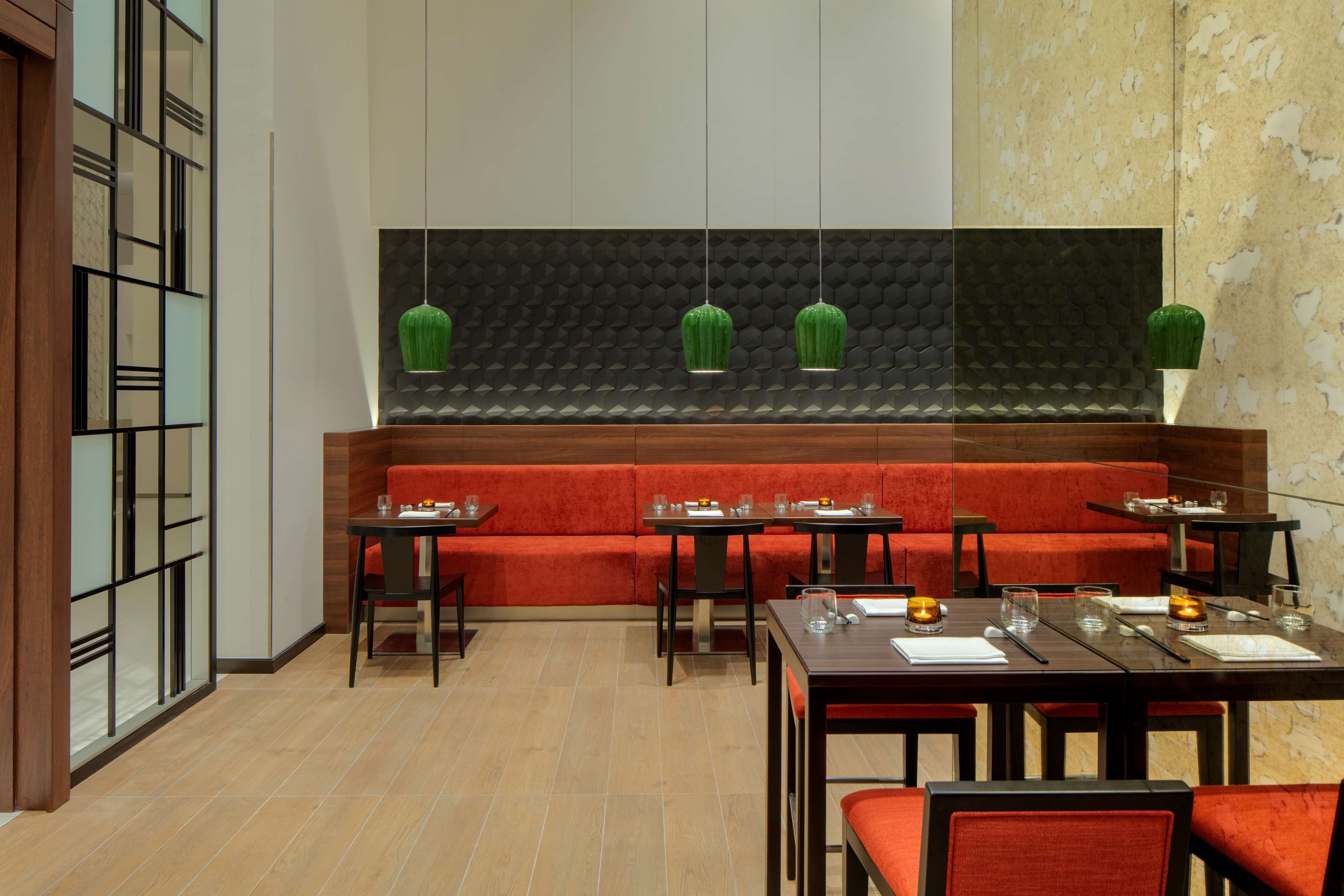 Restaurante com assentos vermelhos, várias mesas, luminárias pendentes verdes e parede com textura.