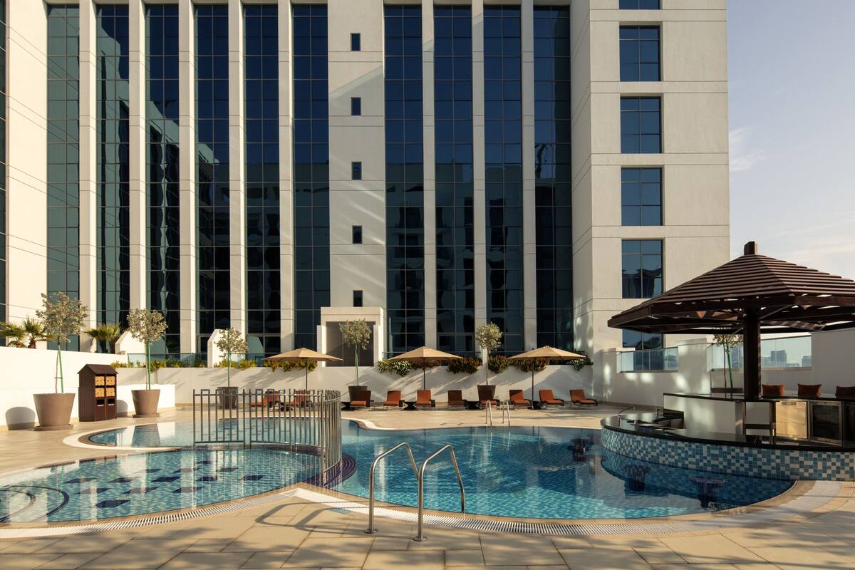 A modern building with a large pool area, including lounge chairs and umbrellas.