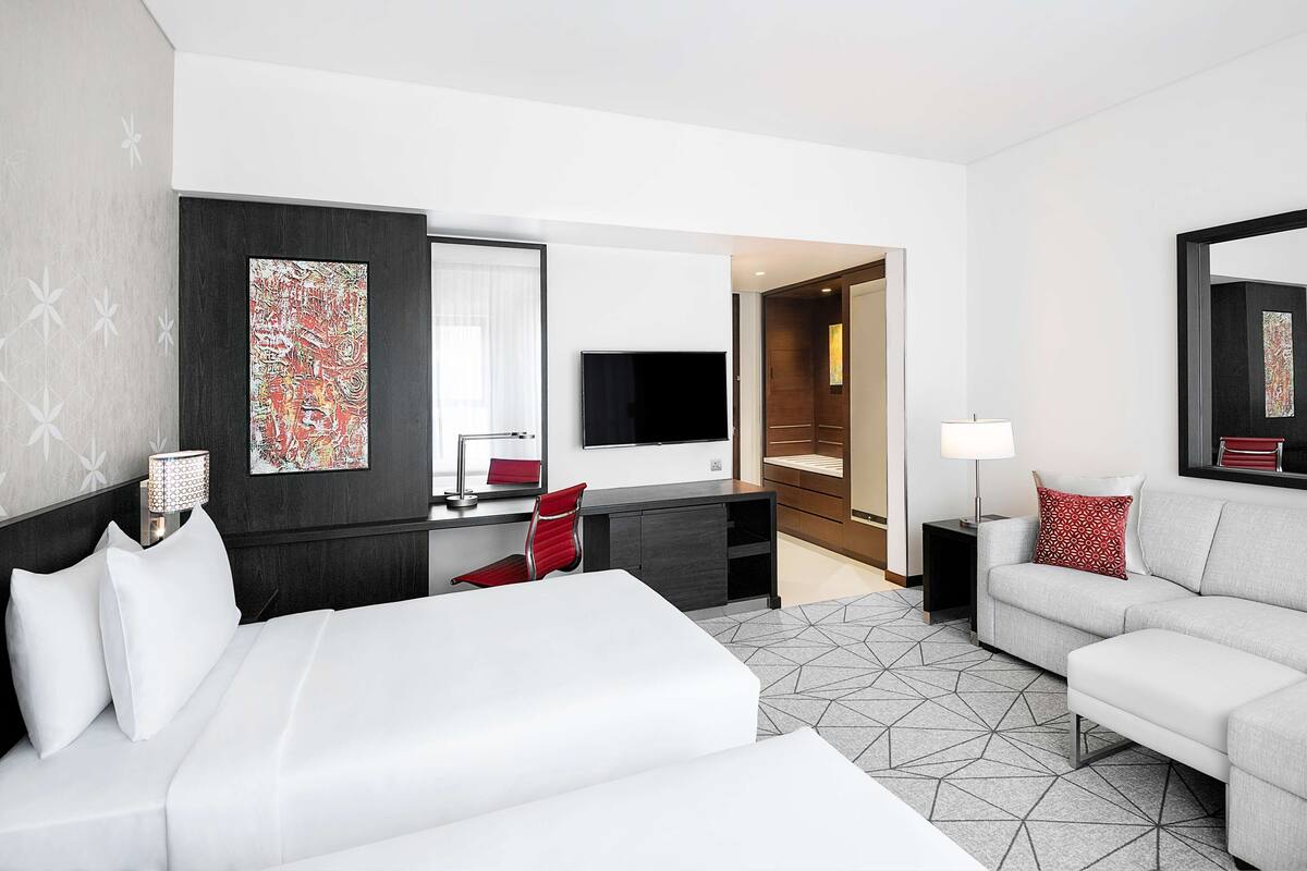 A hotel room with a large bed, a desk, a TV, and a sofa.