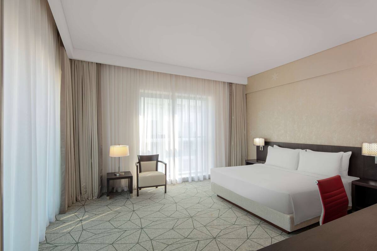 A hotel room with a large bed, a chair, a desk, and a lamp.