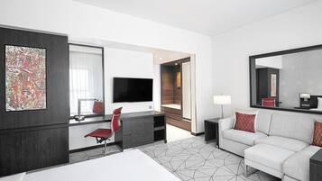 Una habitación de hotel moderna con una cama, un escritorio con una silla, un sofá, un televisor y un espejo grande.