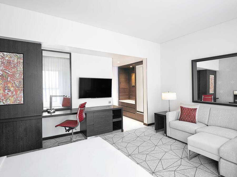 Una habitación de hotel moderna con una cama, un escritorio con una silla, un sofá, un televisor y un espejo grande.