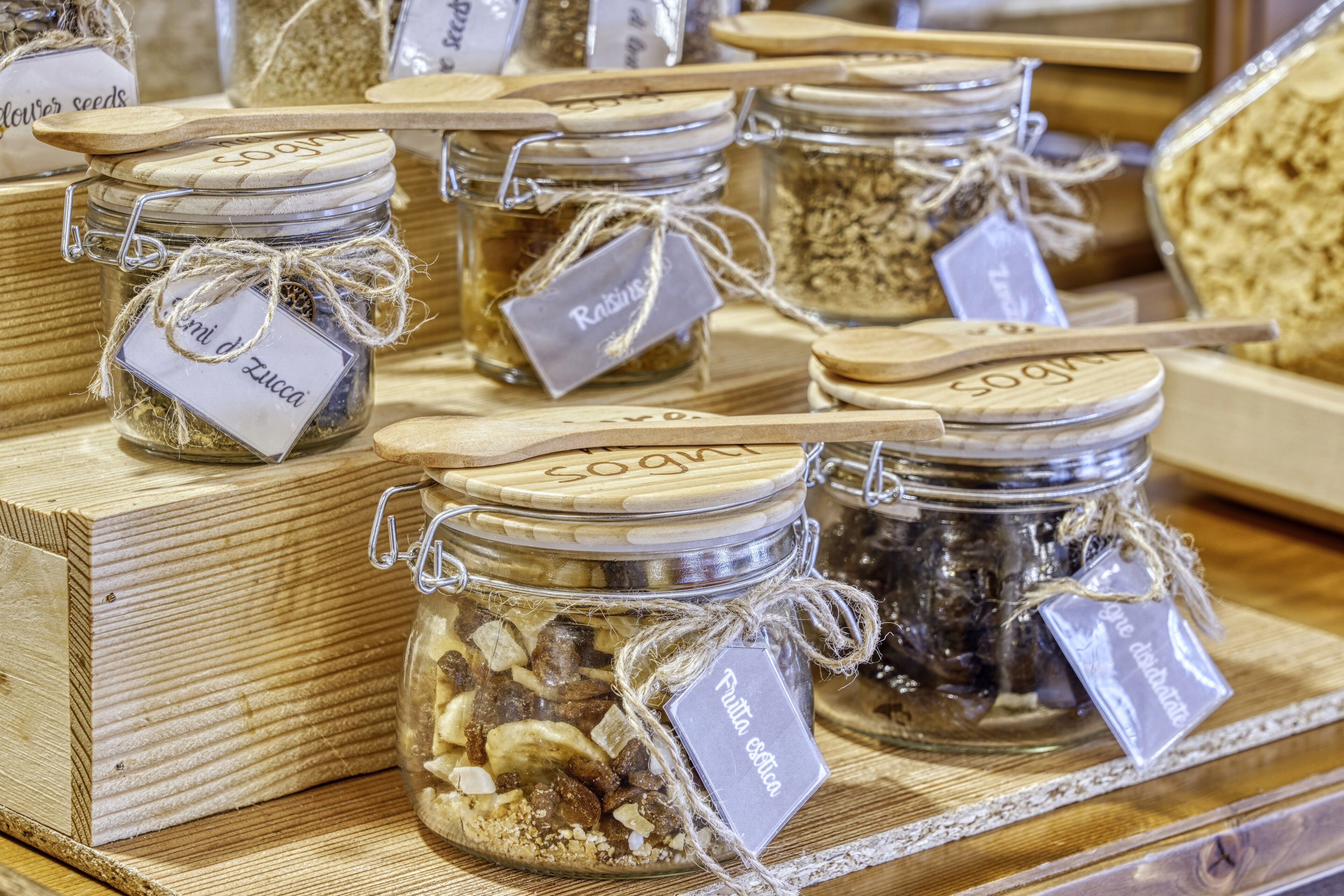 A display of glass jars with labels, each containing different food items, arranged on wooden shelves.
