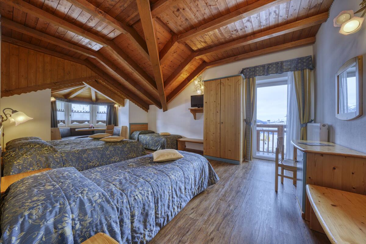 A bedroom with two beds, wooden ceiling beams, a desk, and a view of the outdoors.