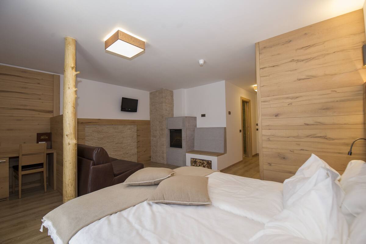 A modern hotel room with a wooden headboard, a large bed with white linens, a brown leather sofa, a wooden desk, and a stone accent wall.