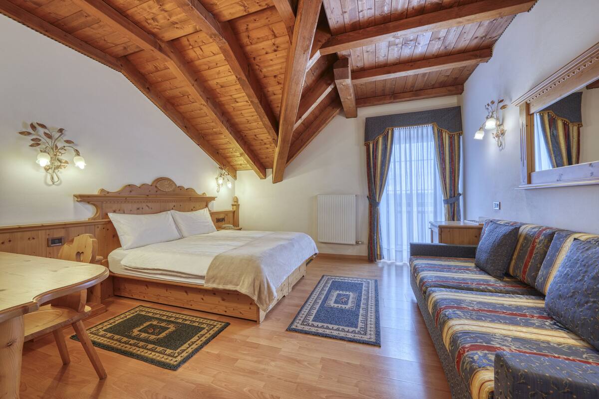 A bedroom with a wooden ceiling, a bed, a sofa, a table, and a chair.