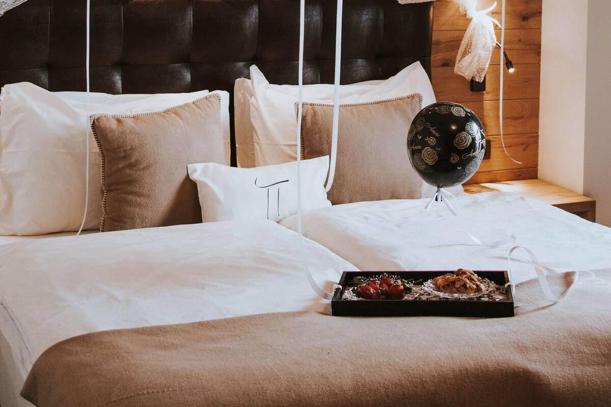 A bedroom with a wooden headboard, white bedding, and a tray with food on the bed.