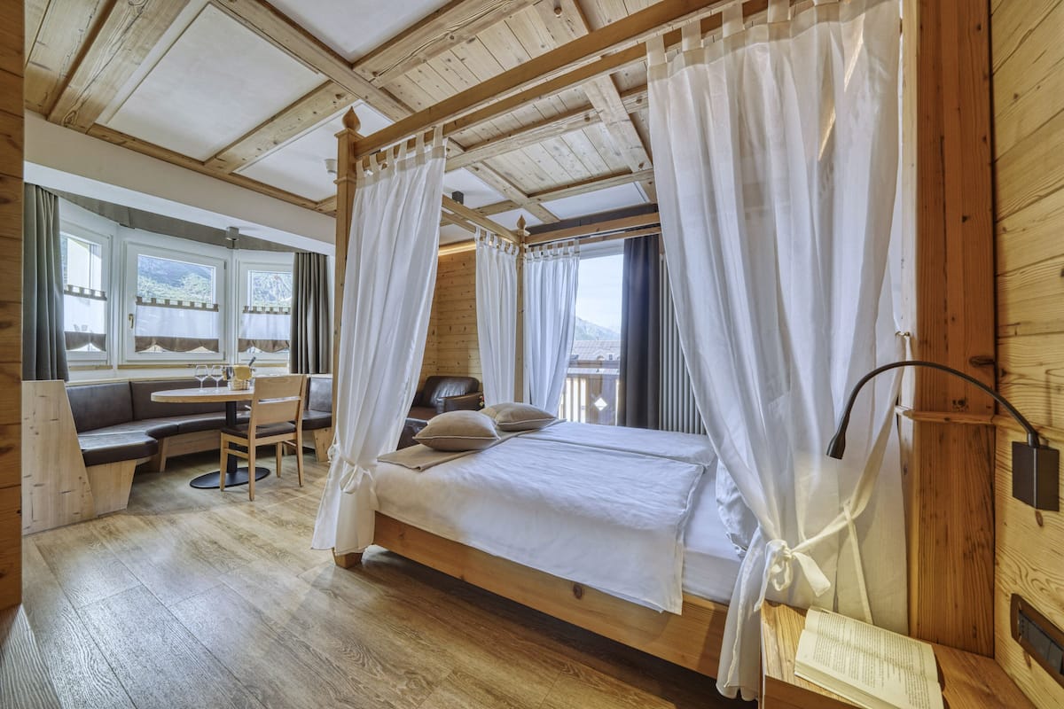 A wooden cabin bedroom with a four-poster bed, a dining table, and a sofa.