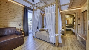 A wooden cabin interior with a four-poster bed, a brown leather sofa, and a bathroom with a bathtub and sink. - Hotel La Torretta (Vermiglio)