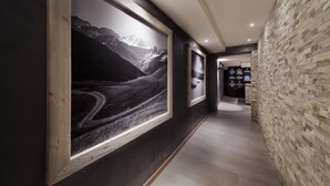 A hallway with framed photographs on the walls, a wooden floor, and a stone wall on one side. - Hotel La Torretta (Vermiglio)