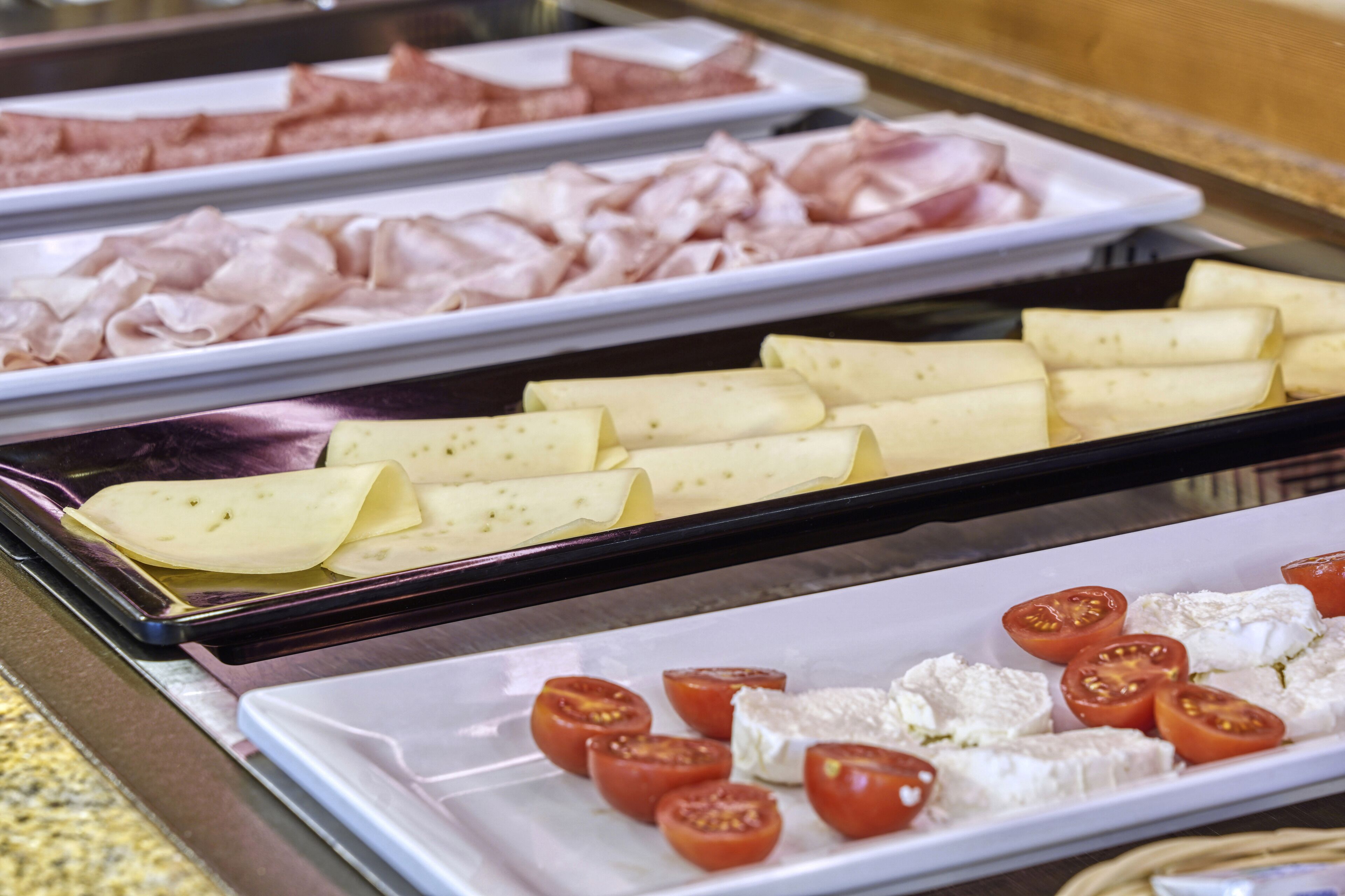 A buffet with various meats, cheeses, and tomatoes.