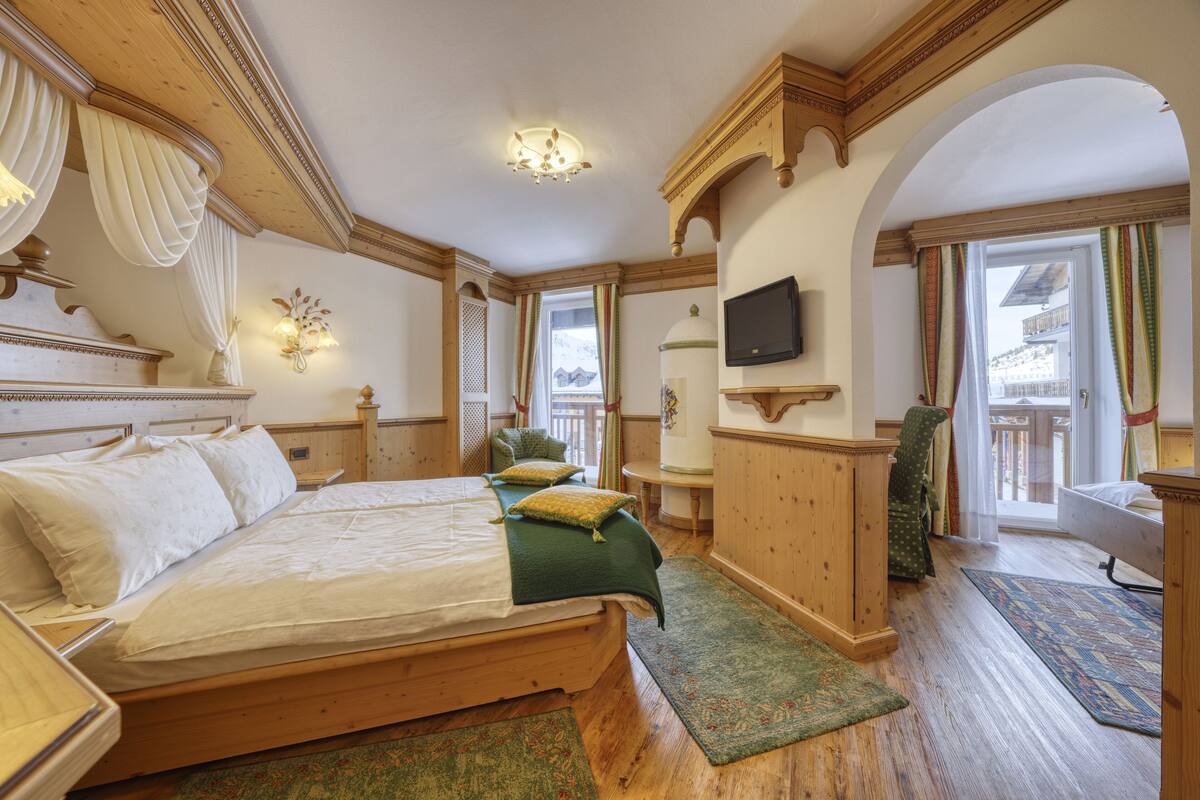A spacious bedroom with a large bed, wooden headboard, and a television mounted on the wall.