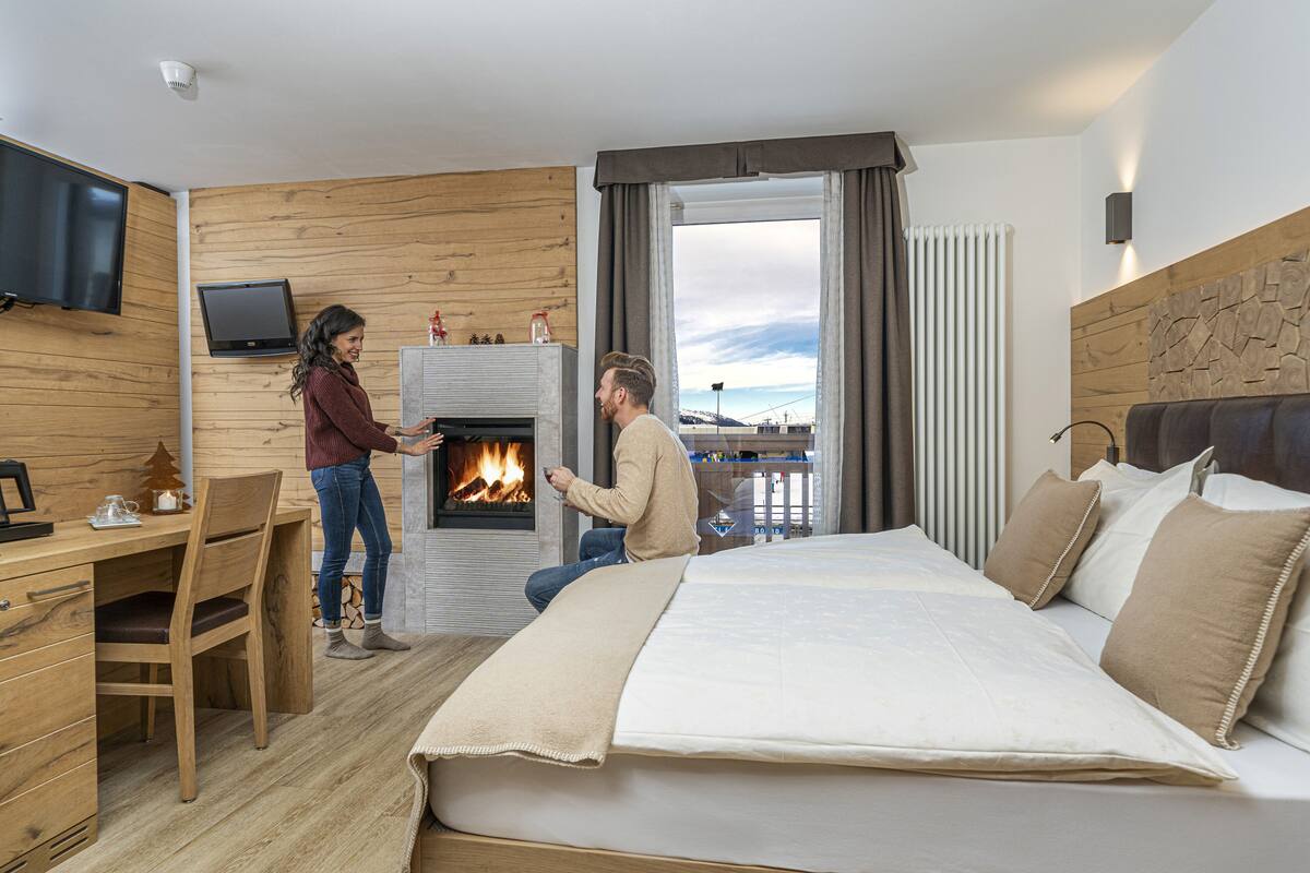 A modern hotel room with a large bed, a fireplace, a desk, and a TV.