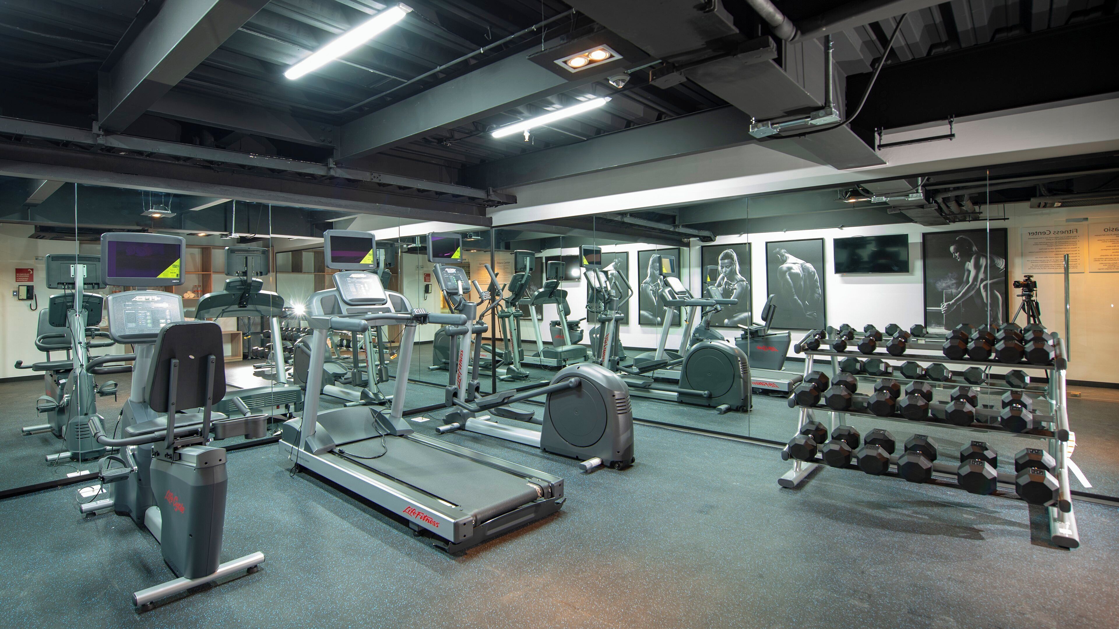 Een fitnessruimte met diverse trainingsapparaten, waaronder loopbanden, hometrainers en gewichten.