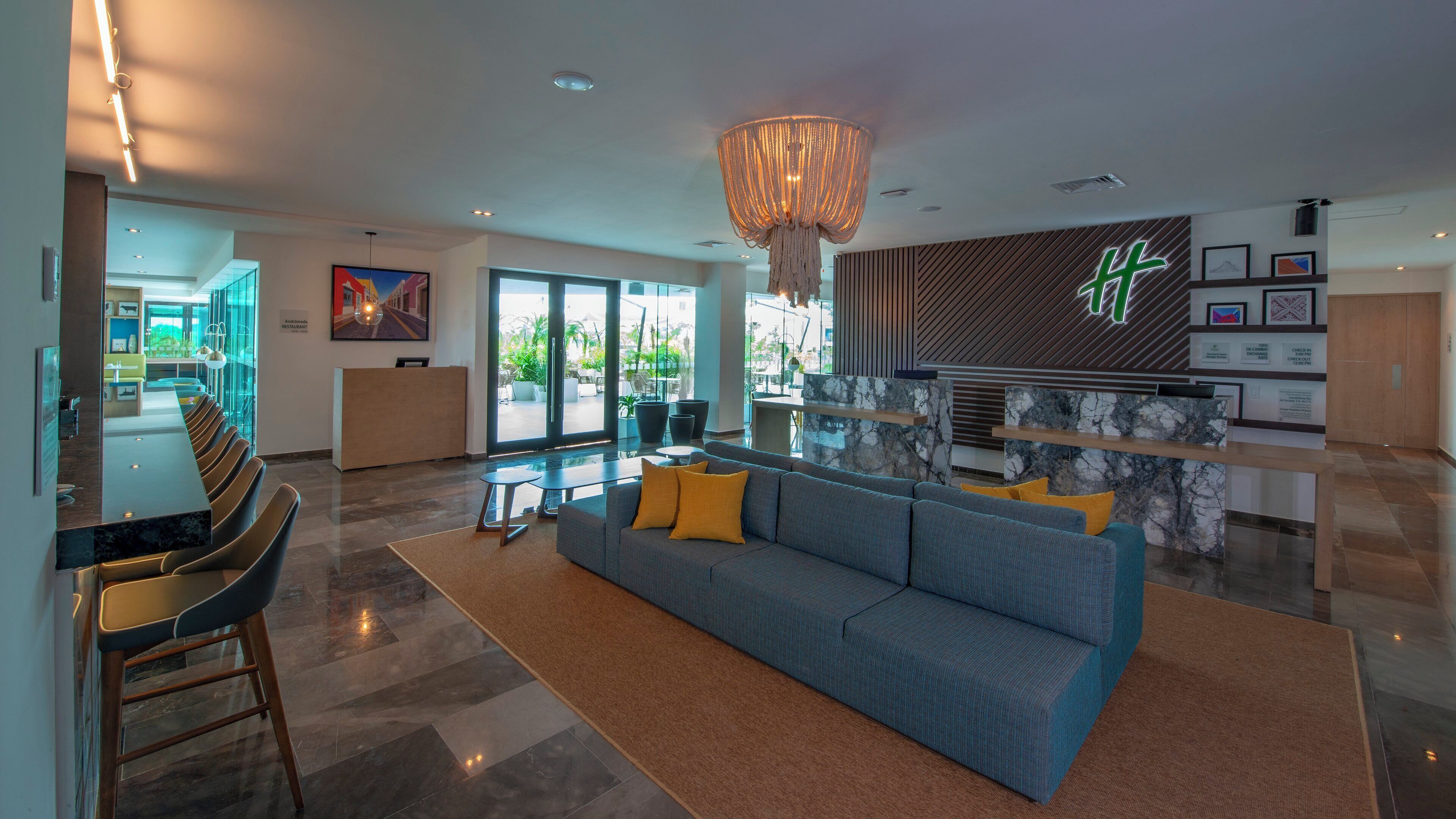 A modern hotel lobby with a reception desk, seating area, and a large chandelier.