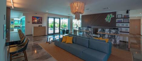 A modern hotel lobby with a reception desk, seating area, and a large chandelier.