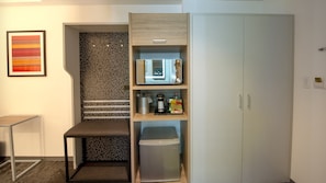 A compact hotel room with a kitchenette, a small seating area, and a wardrobe.