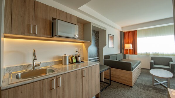 A compact hotel room with a kitchenette, a sofa, a small table, and a window with curtains. - Holiday Inn Hotel & Suites Merida La Isla by IHG (Mérida)