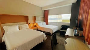 A hotel room with two beds, a desk, a chair, a TV, and a window with curtains.