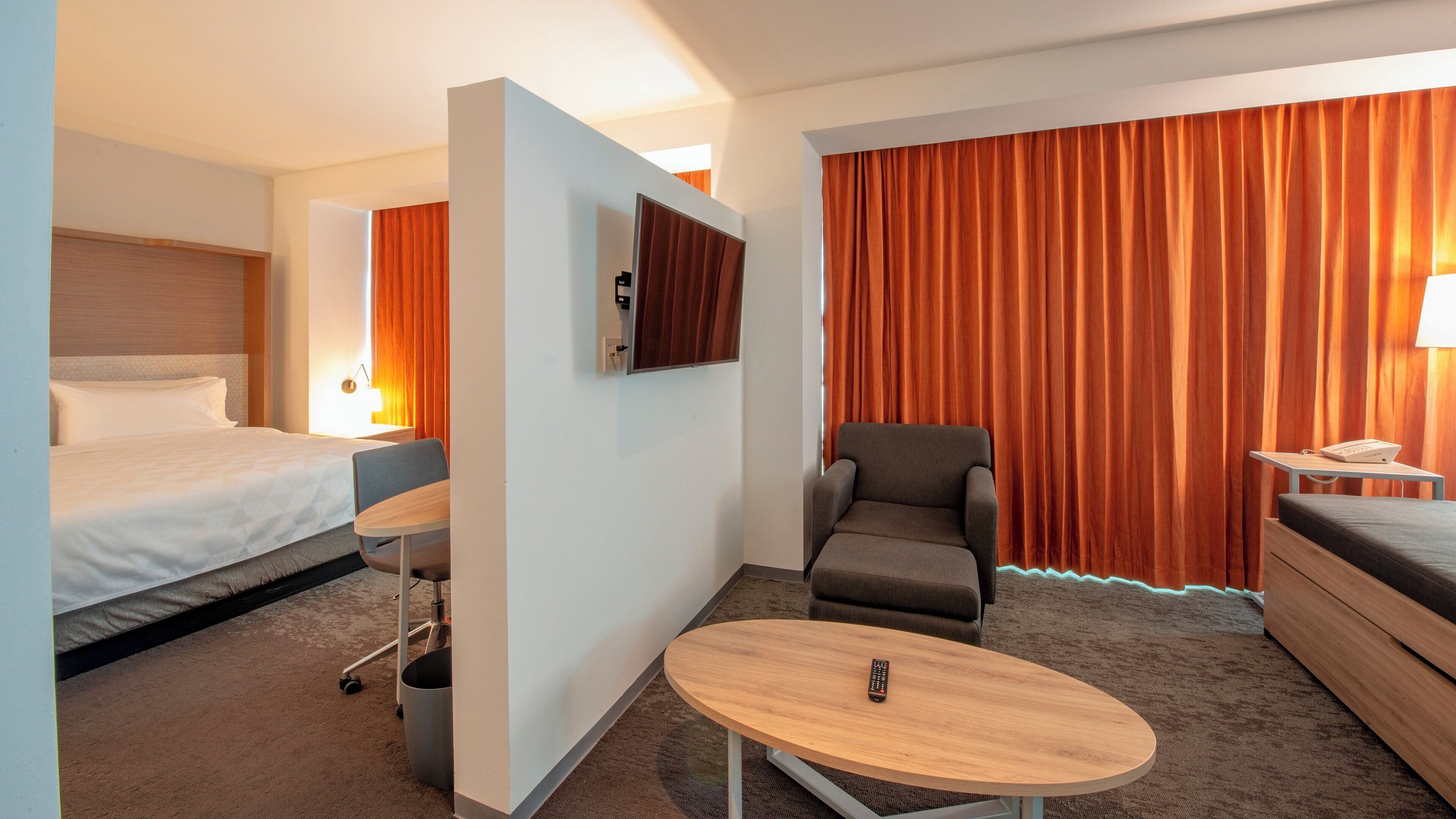 A hotel room with a bed, a desk, a chair, a TV, and a large window with curtains.
