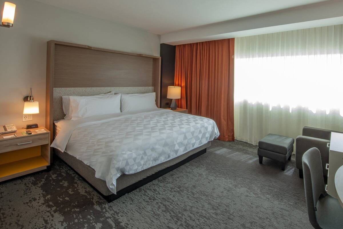 A hotel room with a bed, a desk, a chair, a nightstand, and a lamp.