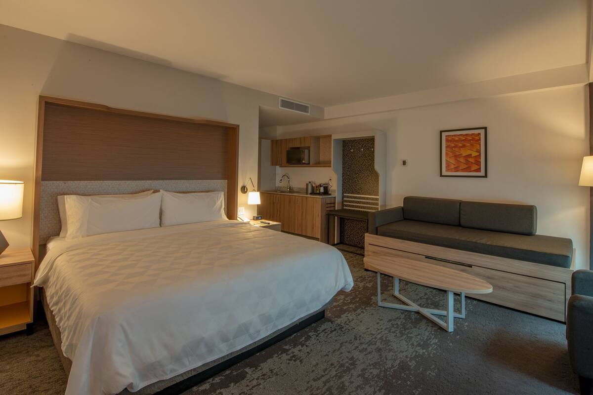 A hotel room with a large bed, bedside tables, a desk, a sofa, and a microwave.